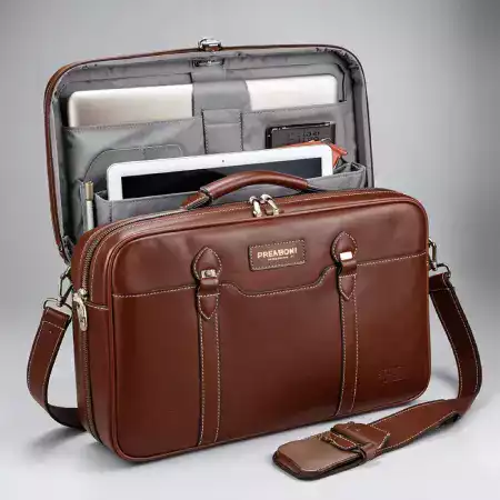 A classic ManBagCo leather satchel resting on a vintage wooden desk with books, evoking timeless academic style